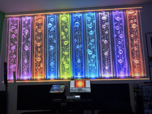 Colorful vertical patterns fill a projection above a desk with a controller and computer screen.