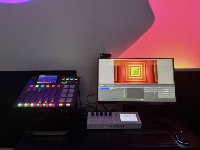 A pad controller, small keyboard and monitor sit together beneath pink and orange wall lighting.